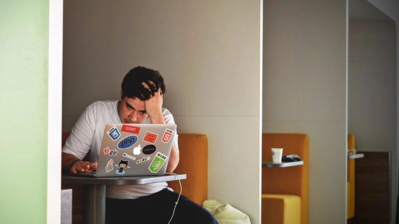 Man sits with his hand on his head in front of a laptop